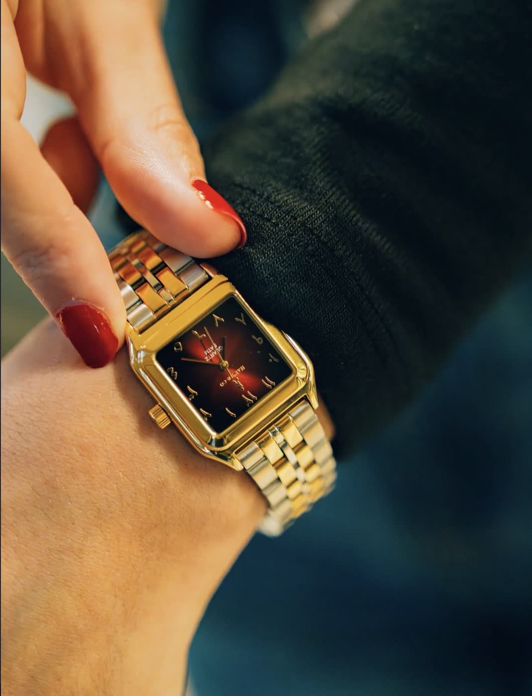 The Queen Piece worn on a wrist: a red dial in a gold-tone square case on a two-tone bracelet